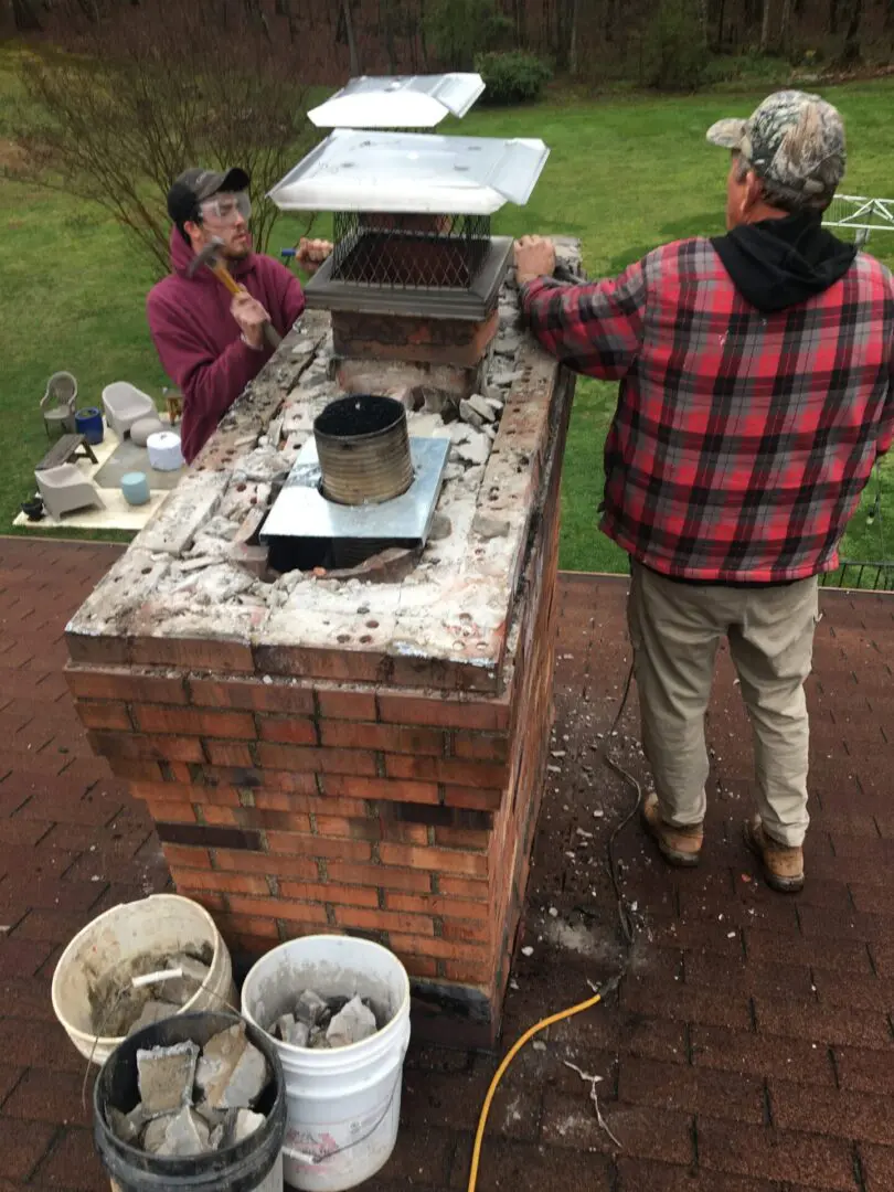 Two people standing around a brick oven with some wood burning.